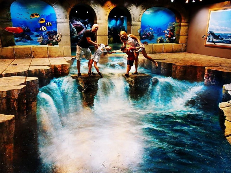 Family at Indoor Water Play Area at Art in Paradise Chiang Mai Family playing on a simulated rocky bridge with water and underwater murals surrounding them at Art in Paradise Chiang Mai.