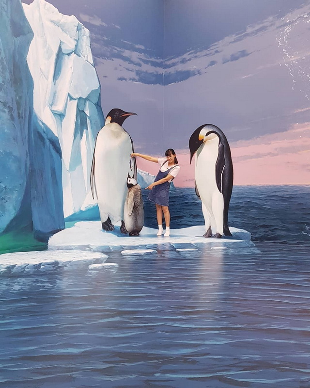 Girl standing on an ice platform with painted penguins and ocean background at Art in Paradise Chiang Mai.