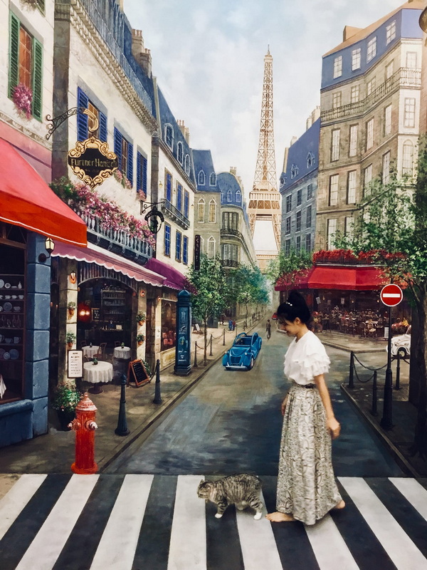 Cityscape with Eiffel Tower at Art in Paradise Chiang Mai Woman and cat crossing street on painting of cityscape with Eiffel Tower in background at Art in Paradise Chiang Mai.