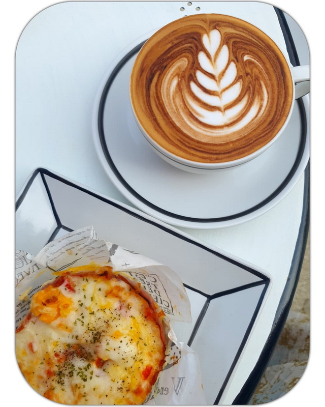 Latte with latte art and a small pizza in a basket on a white table at Chiang Mai Art in Paradise.