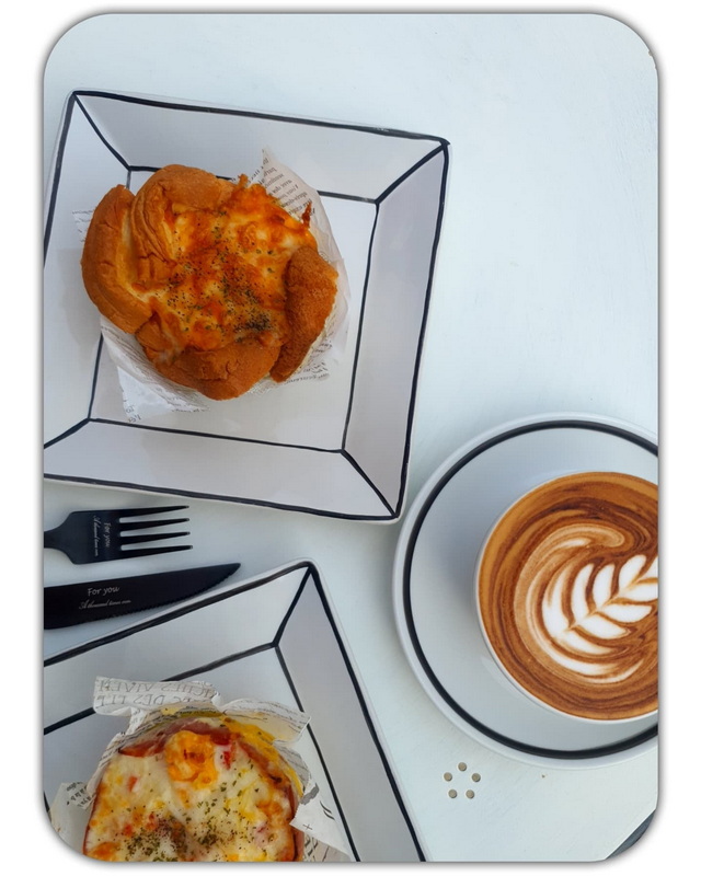 Two pizzas on geometric plates and a latte with leaf pattern on a white table at Chiang Mai Art in Paradise.