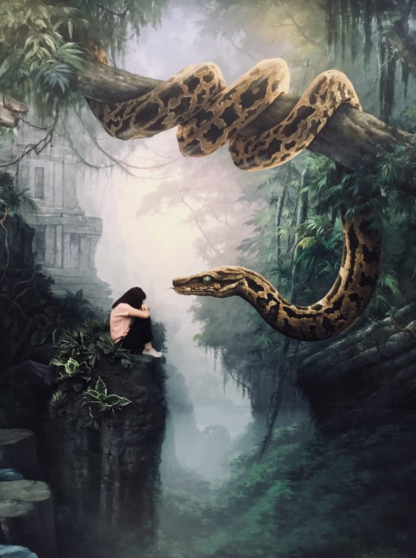 Jungle Art Illustration Scene at Art in Paradise Chiang Mai Person sitting on rocks in jungle mural with large painted snake hanging from tree branch at Art in Paradise Chiang Mai.