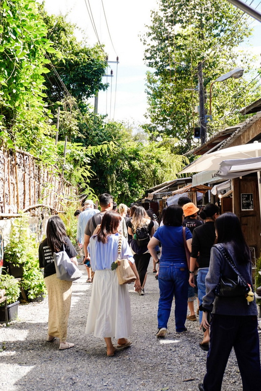 Busy Market Pathway at Baan Kang Wat People strolling along a tree-lined pathway with small shops on the side at Baan Kang Wat.