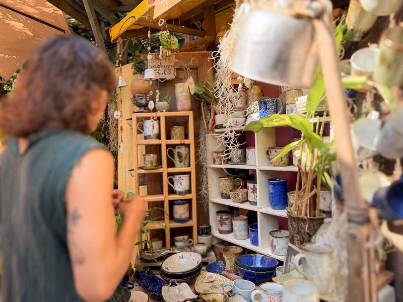 Market Stall with Pottery Collection at Baan Kang Wat Woman shopping at a market stall filled with handmade pottery and ceramics at Baan Kang Wat.