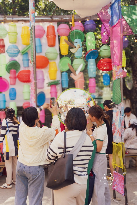 People admiring colorful hanging lanterns and paper decorations outdoors at Baan Kang Wat.