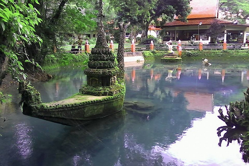 Small temple-like structure on a boat-shaped island with water and trees nearby at Chiang Dao Cave.