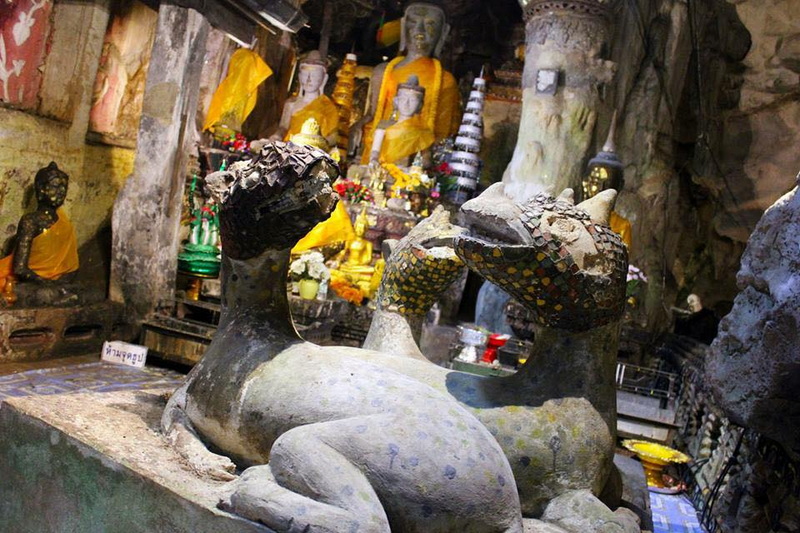 Religious statues and Buddha figures inside a cave with colorful offerings at Tham Chiang Dao.