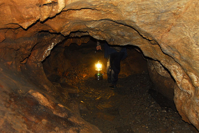 Cave Exploration Scene at Tham Chiang Dao Person inside a dark, narrow underground cave with a lantern on the floor at Tham Chiang Dao.