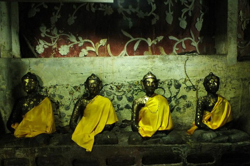 Four black statues with yellow cloths seated in front of floral wall design at Chiang Dao Cave.