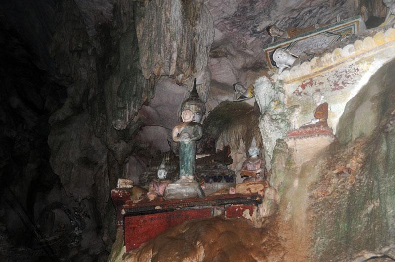 Inside a cave with statues and wall paintings, dimly lit at Tham Chiang Dao.