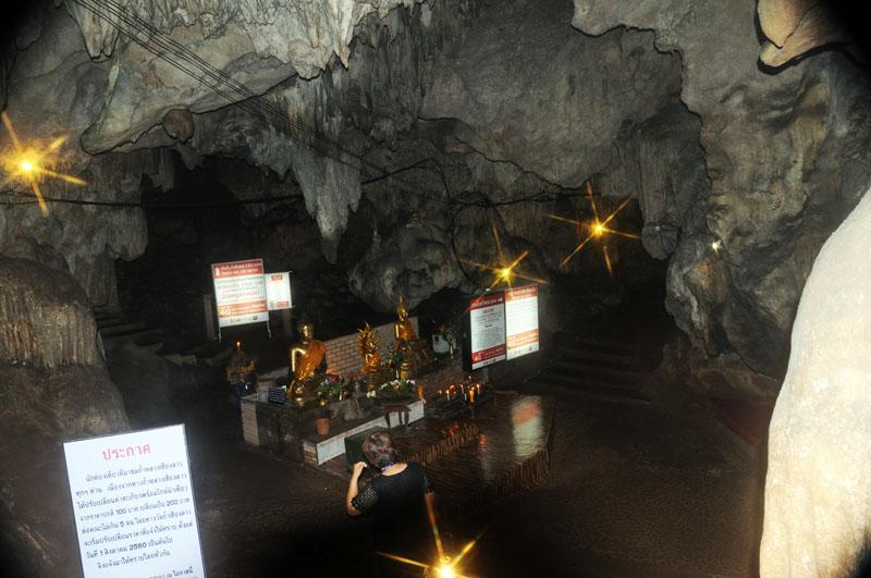 Person sitting near Buddhist statues inside Chiang Dao Cave with informational signs at Tham Chiang Dao.