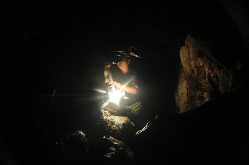 Person inside a dark cave holding a flashlight, with rocky walls around them at Tham Chiang Dao.