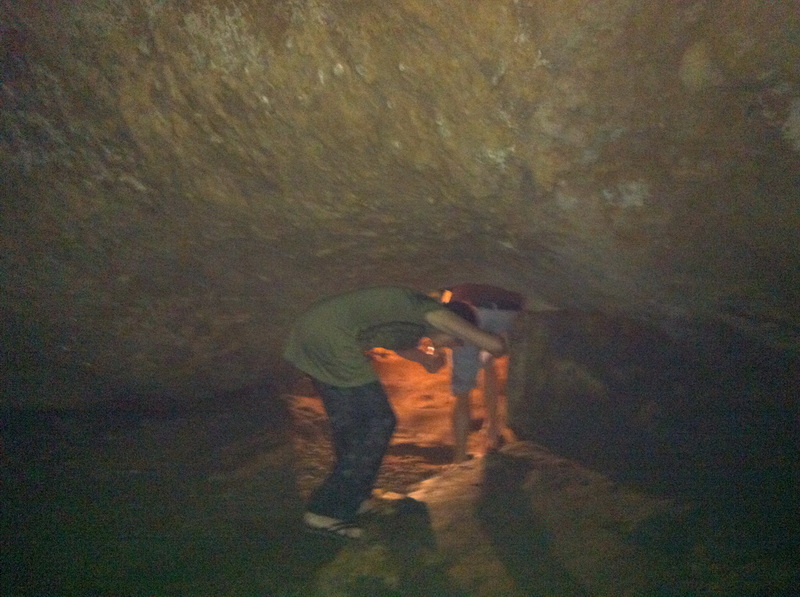Person exploring inside a dark cave with a flashlight illuminating the area at Tham Chiang Dao.