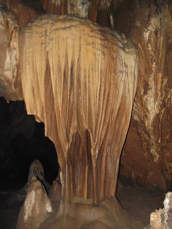 Large stalactite hanging inside a dark cave with person's feet visible at Chiang Dao Cave.