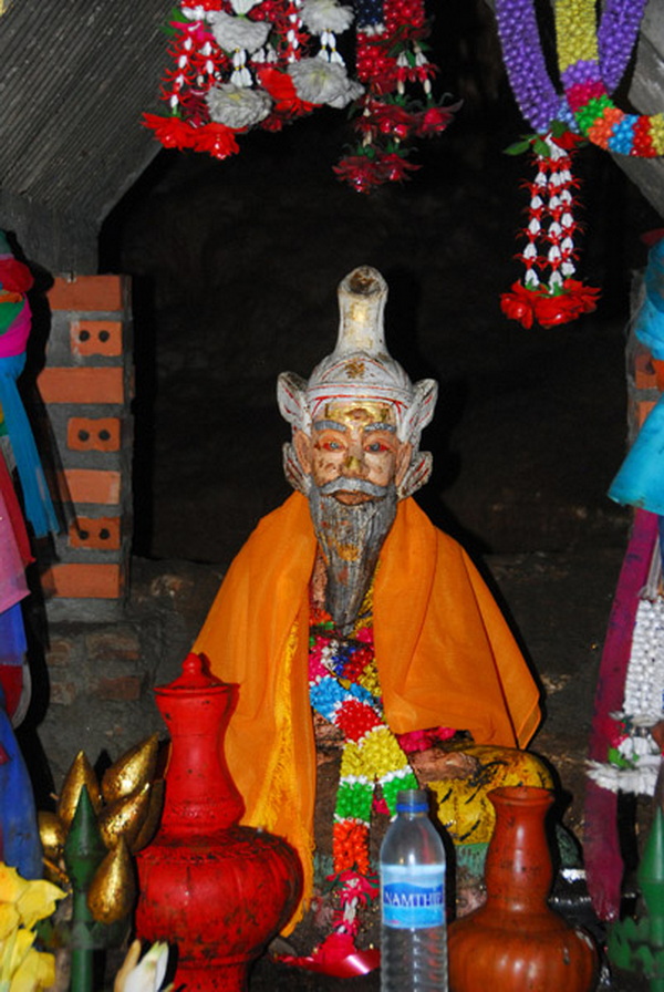 Statue of an elderly man with traditional attire inside a cave surrounded by colorful decorations at Tham Chiang Dao.
