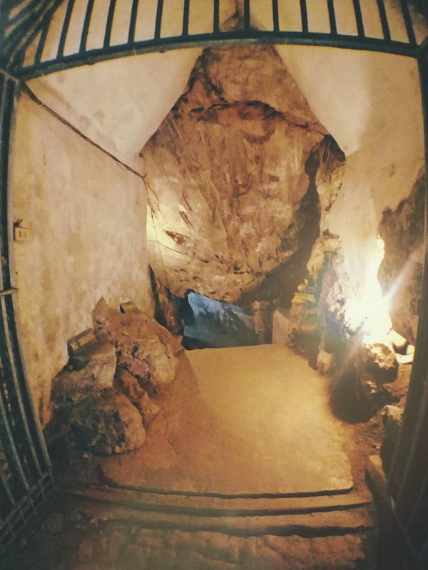 Gated entrance to a cave with rocks and warm interior lighting at Tham Chiang Dao.