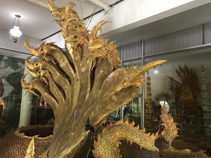 Intricate golden dragon sculpture with multiple heads inside a building exhibit at Mueang On Cave.