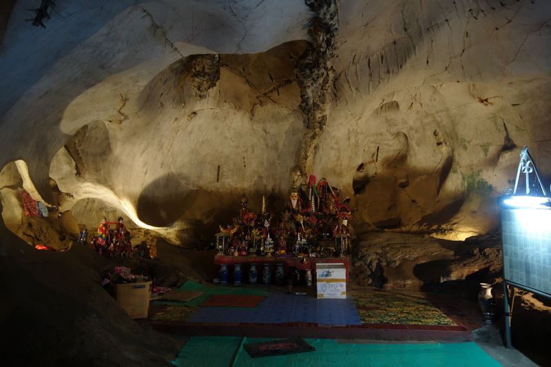 Interior cave with statues and offerings on a platform inside a rock chamber at Mueang On Cave.