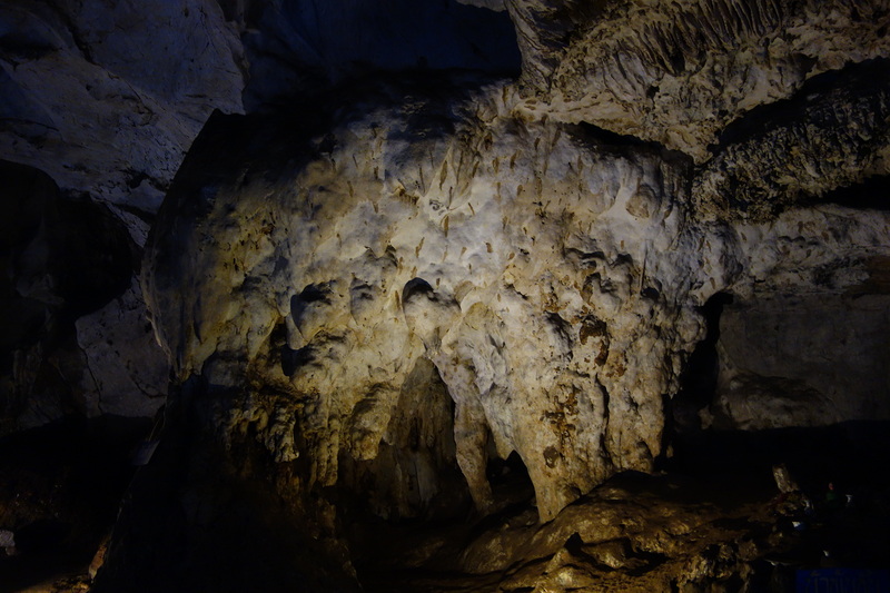 Dark limestone cave interior with stalactites and stalagmites illuminated by lights at Mueang On Cave.