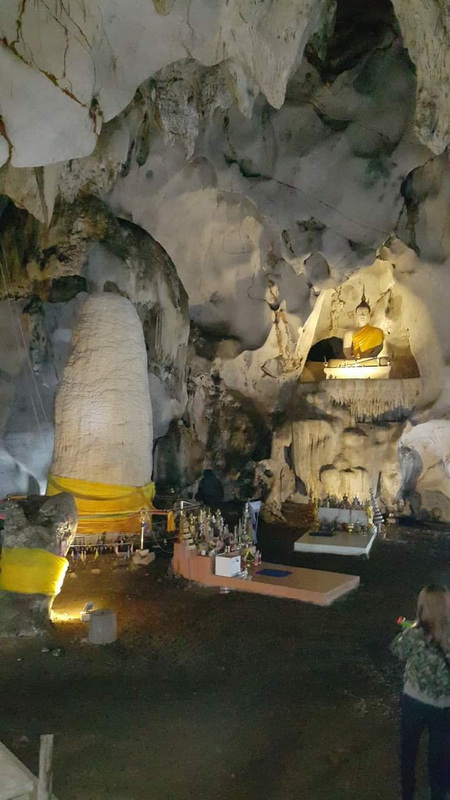 Interior of Mueang On Cave Buddha statue inside a cave with offerings and rock formations around at Mueang On Cave.