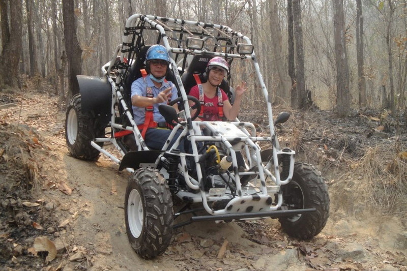 Two children in helmets riding an off-road vehicle in a forest trail, surrounded by trees and dry leaves at Chiang Mai atv tour.