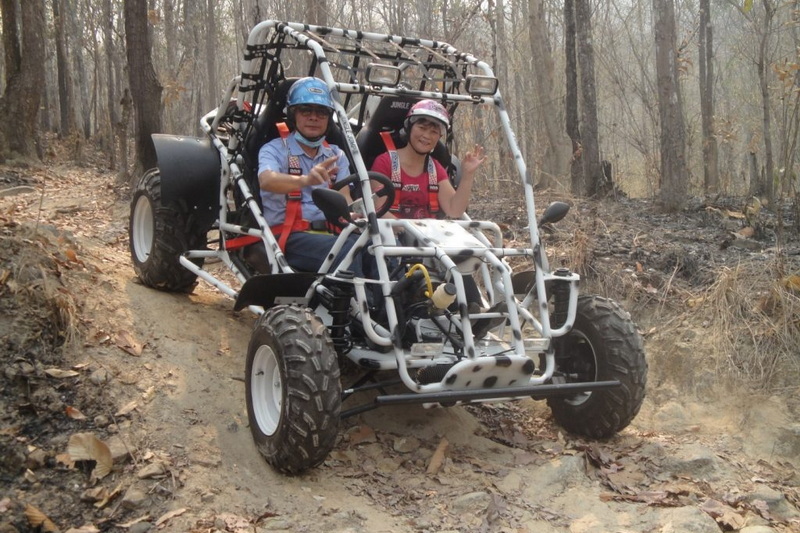 Children riding an ATV through a dry, wooded trail during daytime at ATV tour Chiang Mai.