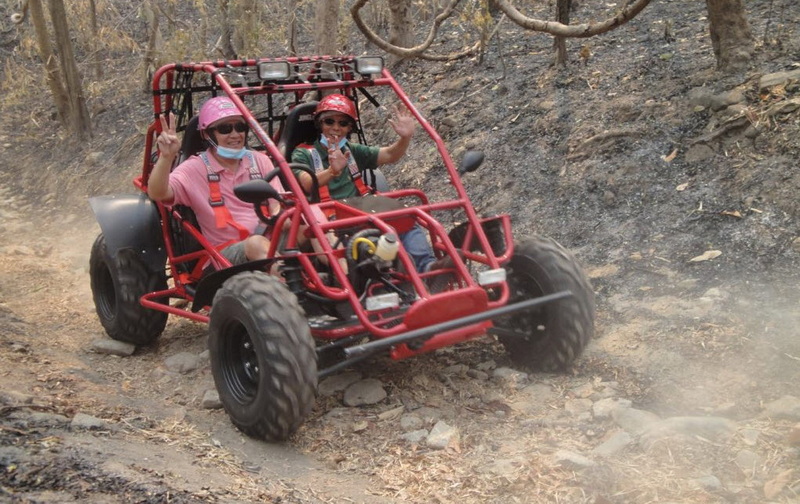 Two women in sunglasses riding a red ATV on a dusty forest trail at Chiang Mai Adventure Tours.