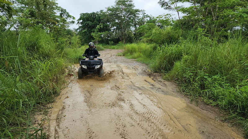 Person riding an ATV on a muddy trail amidst lush green surroundings at Chiang Mai atv tour.