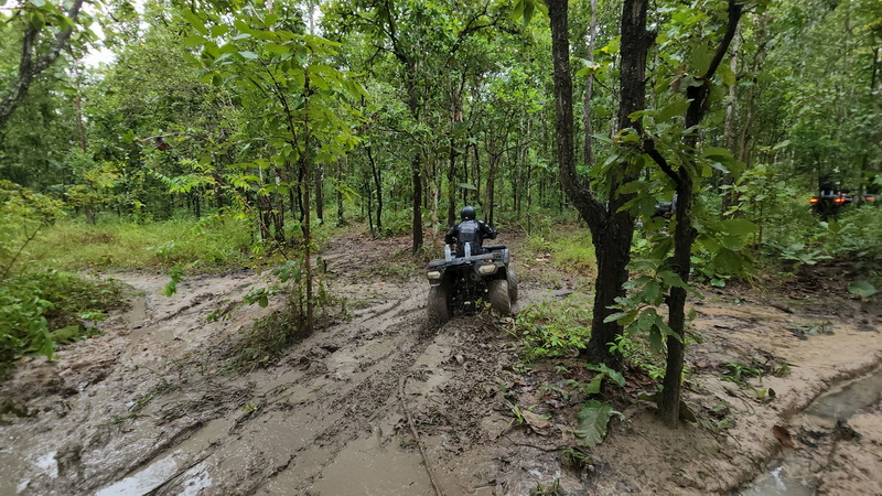Person riding ATV through muddy forest trail surrounded by green trees at ATV tour Chiang Mai.
