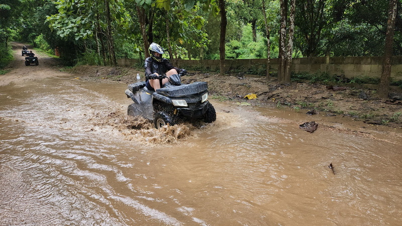 Person riding an ATV through muddy water on forest trail in Chiang Mai at Chiang Mai atv tour.