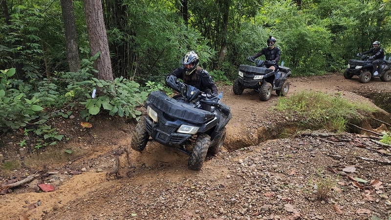 Three riders navigating a rugged forest trail on ATVs surrounded by greenery at ATV tour Chiang Mai.