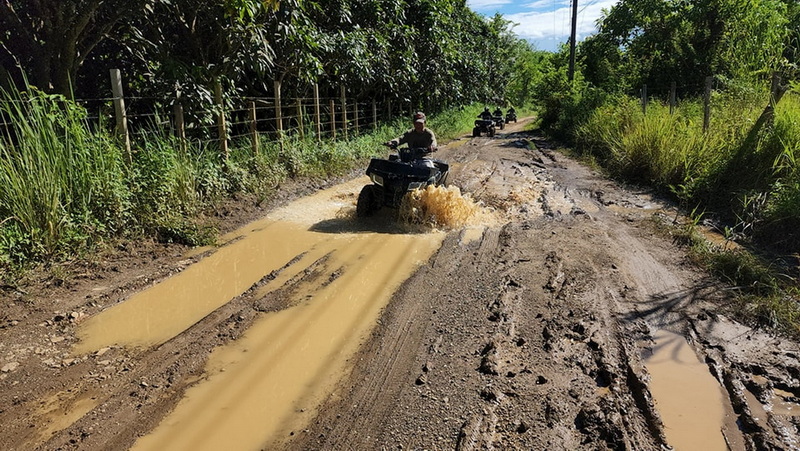 ATV riders navigating a muddy trail surrounded by lush green trees at Chiang Mai atv tour.