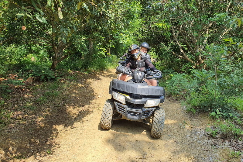 Two riders on an ATV navigating a forest trail covered with greenery at ATV tour Chiang Mai.