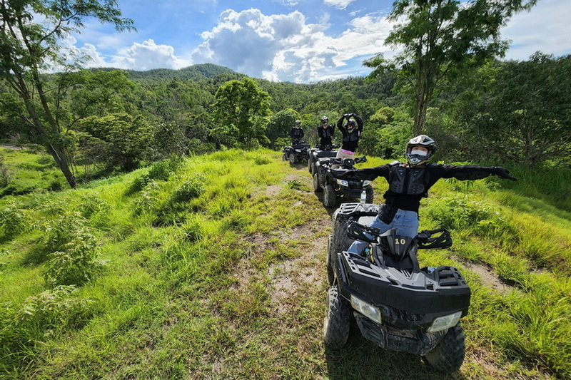 ATV Adventure in Nature at Chiang Mai atv tour Group of ATV riders in helmets and masks on a grassy trail with trees and hills in background at Chiang Mai atv tour.