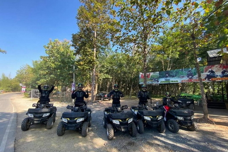 Five ATV riders wearing helmets and gear on a forest trail under a blue sky at Chiang Mai atv tour.