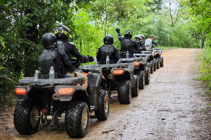 Group of ATV riders in helmets and gear navigating a forest trail at Chiang Mai atv tour.