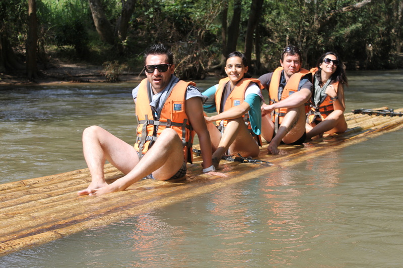 Group of four people on bamboo raft floating on river with trees in background at Rafting in Mae Wang.