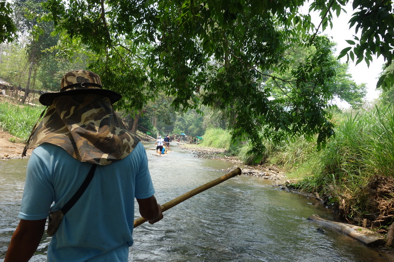 Person paddling bamboo raft through lush river surrounded by trees at Rafting in Mae Wang.