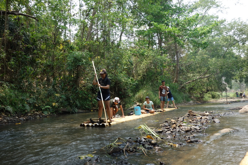 People on a bamboo raft floating on a river with lush green trees all around at Rafting in Mae Wang.