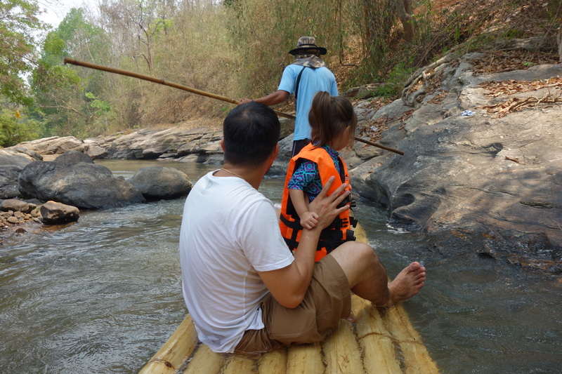 A man and girl sitting on a bamboo raft in a rocky river surrounded by trees at Rafting in Mae Wang.