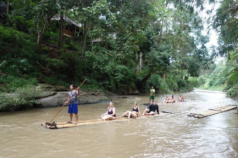 Group on bamboo raft sailing down a lush green river surrounded by trees at Bamboo Rafting in Mae Wang.