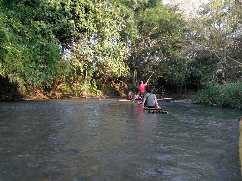 People crossing a river on bamboo rafts surrounded by trees at Rafting in Mae Wang.