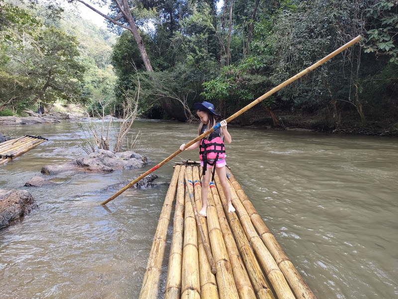 Bamboo Rafting Adventure at Bamboo Rafting in Mae Wang Girl balancing on bamboo raft holding a pole in a forest river scene at Bamboo Rafting in Mae Wang.