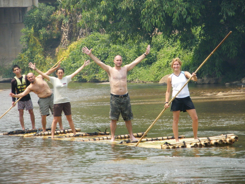 Group of five people on a bamboo raft floating in a river surrounded by lush greenery at Rafting in Mae Wang.