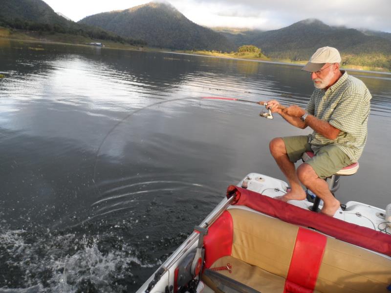 Man sitting on boat fishing on a tranquil lake with mountains in the background at Chiang Mai Fishing.