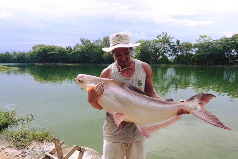 Fishing Adventure at Chiang Mai Fishing Person smiling while holding a large fish by a tranquil lake during daytime at Chiang Mai Fishing.