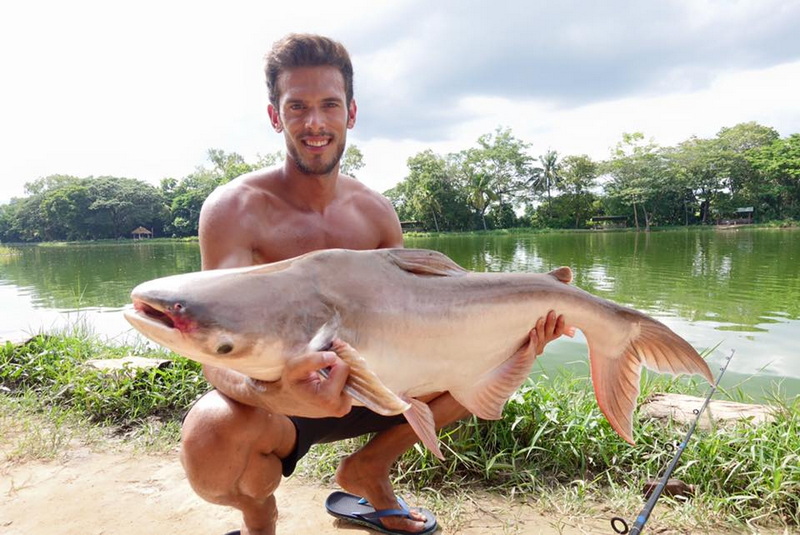Man kneeling by a lake holding a large fish and smiling at the camera at Chiang Mai Fishing Park.