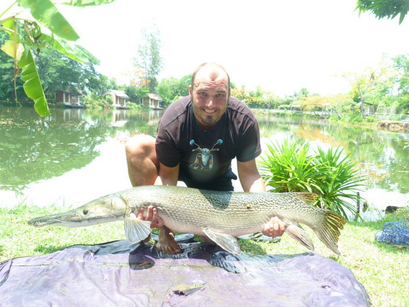 Fishing Success by the Pond at Chiang Mai Fishing Park Man crouching by a pond holding a large fish on a cloth amidst greenery at Chiang Mai Fishing Park.