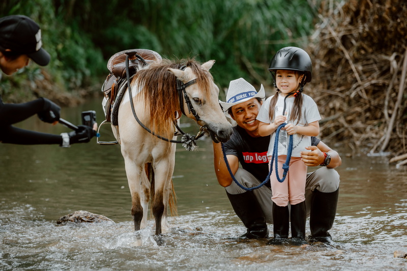 Horse Riding Adventure in Chiang Mai at Horse Riding Chiang Mai Girl in helmet and adult standing with horse in shallow river water at Horse Riding Chiang Mai.