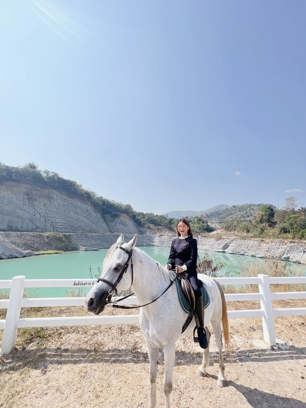 Woman riding a white horse near a turquoise water reservoir and cliffs at Horse Riding Chiang Mai.